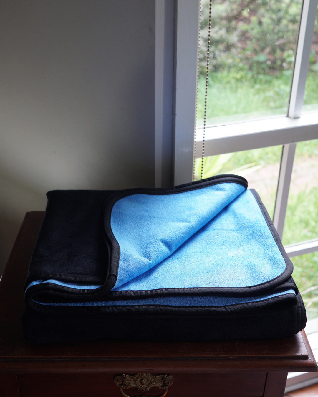 Folded black and blue waterproof blanket beside a window