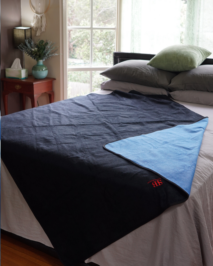 Black side of the waterproof blanket on a bed with blue corner folded back
