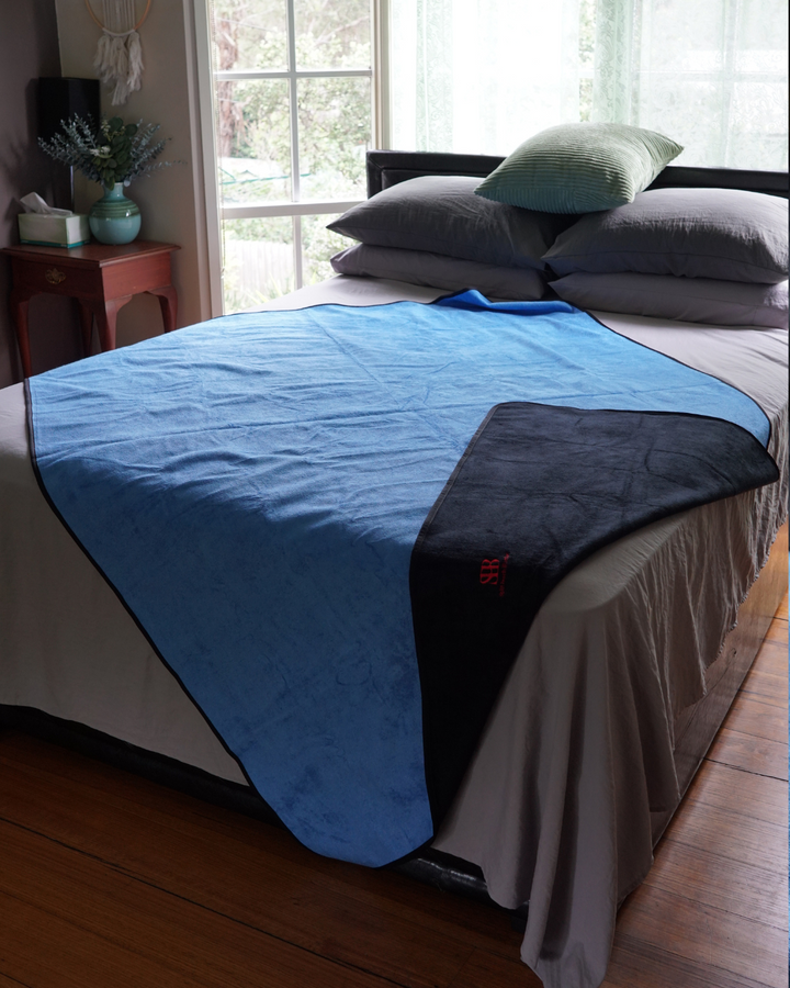 Blue side of the reversible black and blue waterproof blanket spread on a bed with black corner folded back