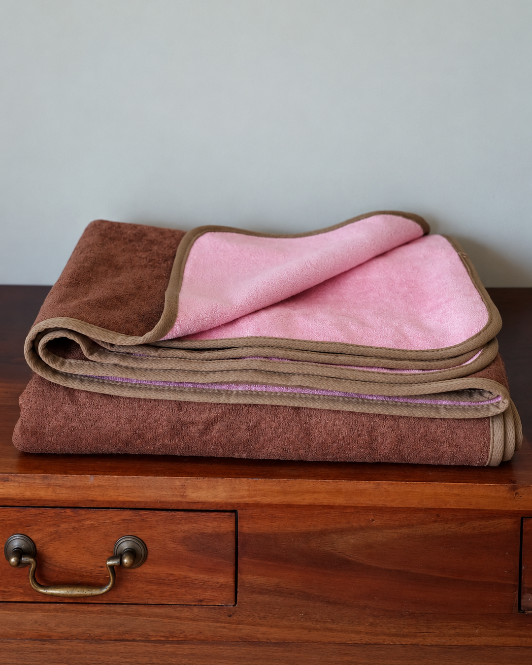 Folded Coffee and Pink bamboo and cotton waterproof blanket showing both sides on a wooden dresser