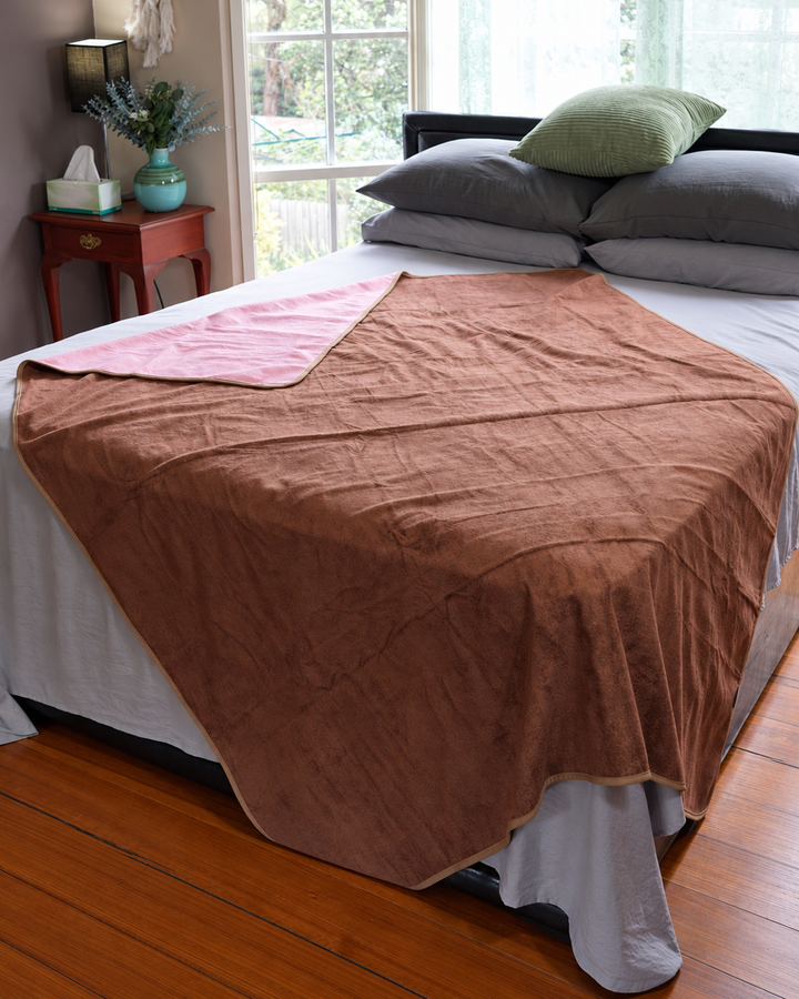 Coffee side of the reversible waterproof blanket on a bed with Pink underside turned back