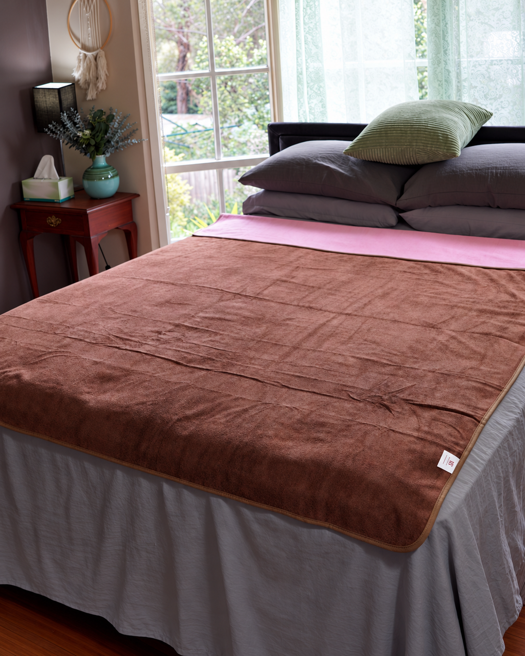 Coffee waterproof blanket laid flat across a bed with Pink reverse folded back
