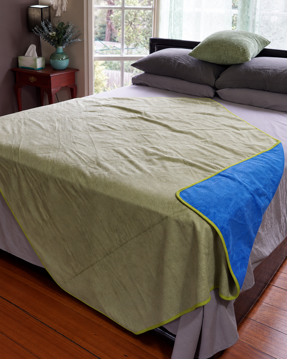 Matcha Mist side of the reversible waterproof blanket on a bed with Capri Blue corner turned back