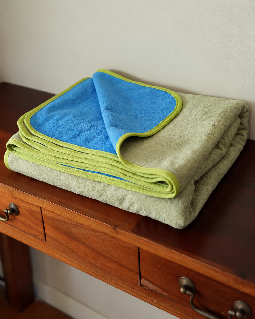 Angled view of the folded Matcha Mist and Capri Blue waterproof blanket