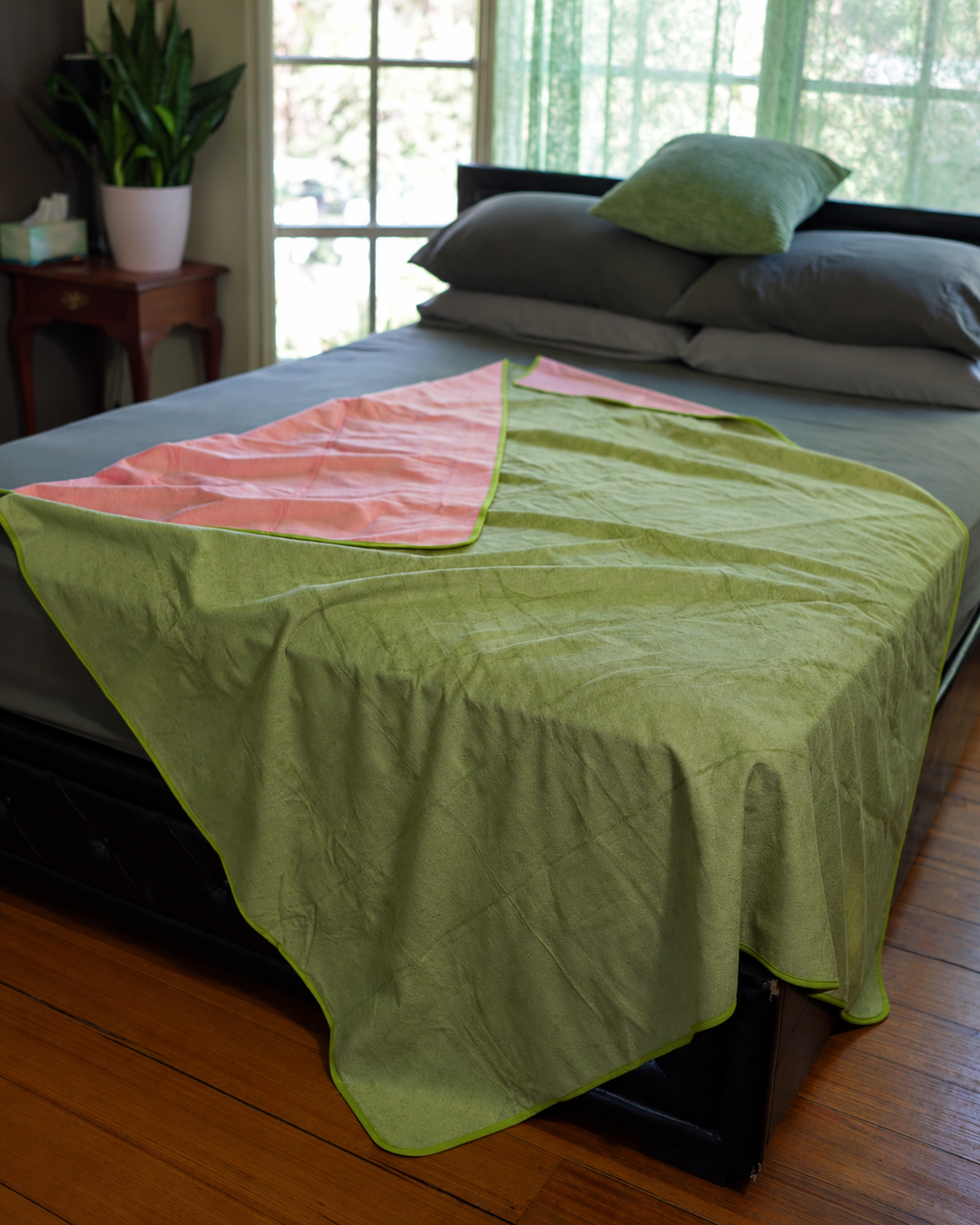 Matcha Mist side of the reversible waterproof blanket spread across a bed with Pink reverse visible