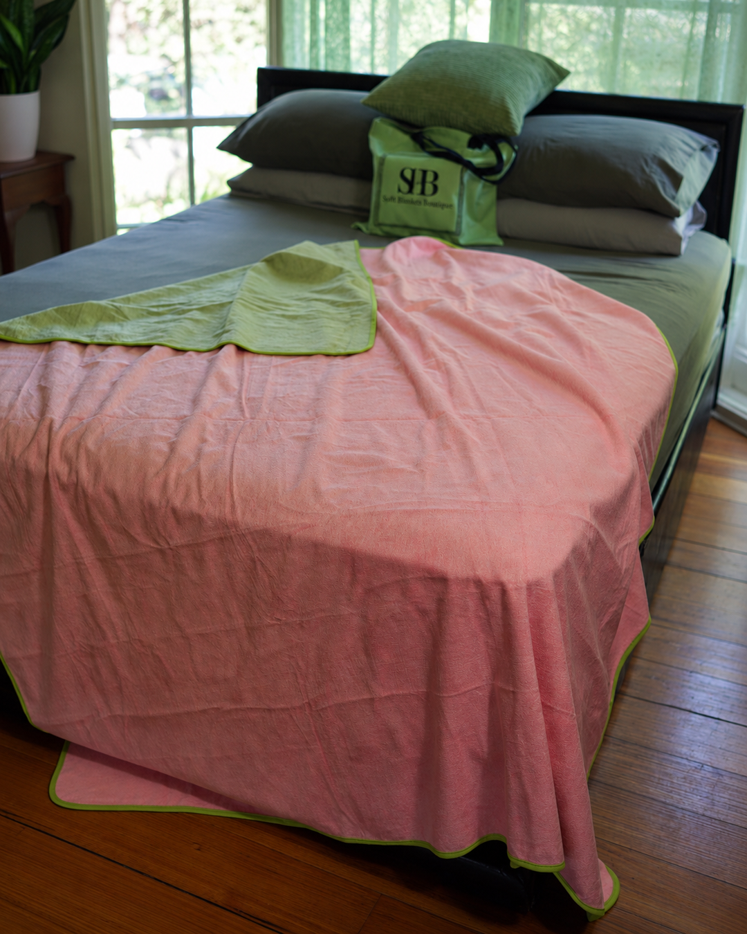 Pink side of the waterproof blanket draped over a bed with Matcha Mist corner turned back